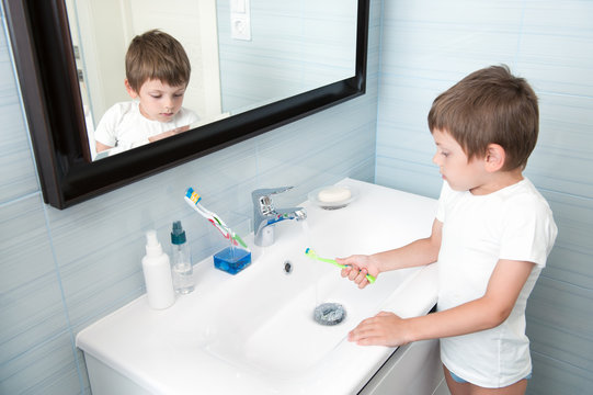 cute small child washing his toothbrush under stream of water in bathroom