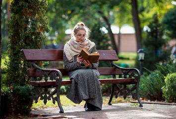 Счастливая старшая женщина, чтение книги в осеннем парке