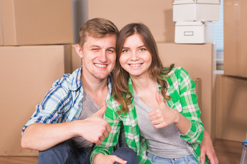 Moving to a new house and repairs in the apartment. Love couple showing a thumbs up and sitting in an empty apartment among boxes