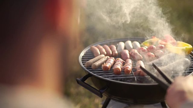 Man roasts sausages on the grill.
