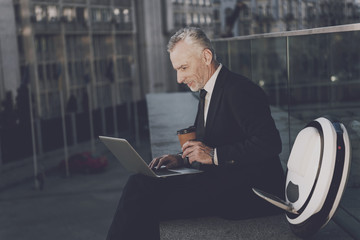 A man is working on a laptop, sitting on a parapet. Near his mono-wheel © Vadym Huzhva