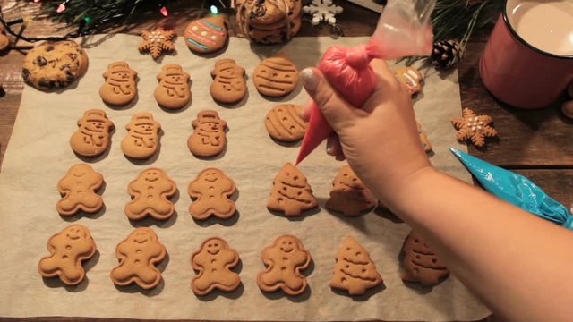Decoration process of Christmas cookies top view. Woman garnishing with icing homemade gingerbread fir trees near festive illuminate pine and cup of latte. Family culinary and traditions concept