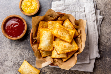 Fried cheese empanadas. Traditional Latin American snack in clay served bowl with chili sauce and mustard. Top view, stone background