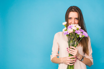 Beautiful young woman holding a bouquet of carnation flowers on a blue background, feminine, celebration