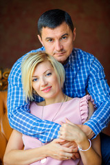 husband tenderly embraces his wife sitting on a chair in his house.
