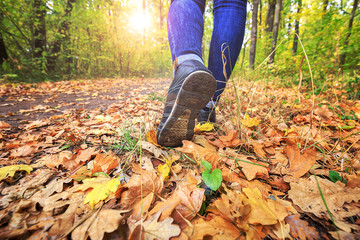 Young girl in jeans and sneakers on his feet, walks through the fall leaves on the road in the woods in the sunshine outdoors