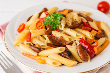 Penne pasta with mushrooms, bell pepper, chilli and parsley on white plate on white wooden background.