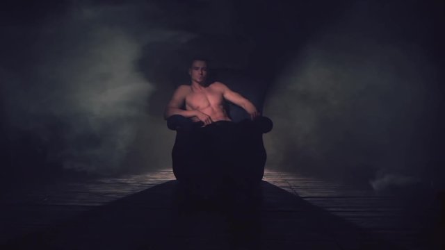 Sexy man sits in an armchair in smoke. The light appears and goes out
