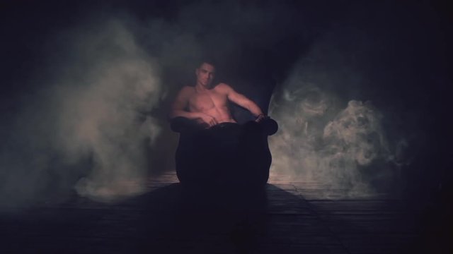 Sexy man sits in an armchair in smoke. The light appears and goes out