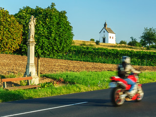 Biker mit Motorrad auf der Landstraße bei Bildstock und Kapelle