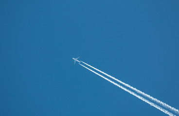 Airplane flying at high altitude leaving its white wake over blue sky