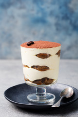 Tiramisu, traditional Italian dessert in glass on a grey stone background. Copy space.