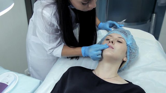 The doctor-cosmetologist introduces Botox into the girl's lips to enlarge them. Lip augmentation in the clinic
