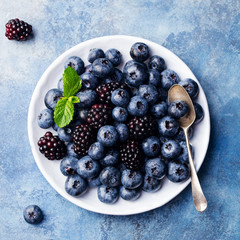 Blueberry and blackberry berries on a white plate on blue stone background. Top view