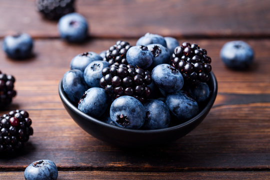 Blueberries, blackberries in black bowl on wooden background