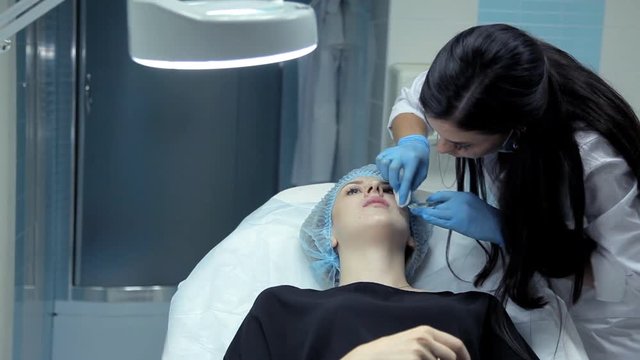 The doctor-cosmetologist introduces Botox into the girl's lips to enlarge them. Lip augmentation in the clinic