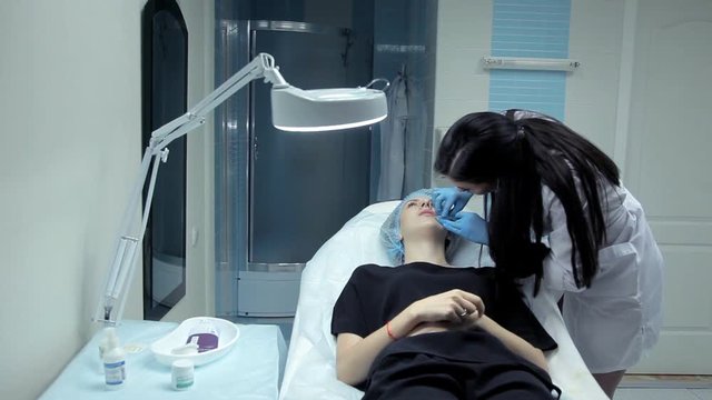 The doctor-cosmetologist introduces Botox into the girl's lips to enlarge them. Lip augmentation in the clinic