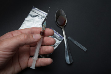 A syringe with a drug in hand on a background of a spoon and packets.
