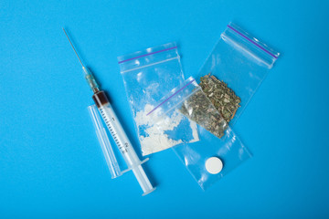 A syringe and a set of illegal drugs in doses on a blue background.