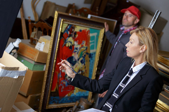 female auctioneer showing her assistant which paintings to take