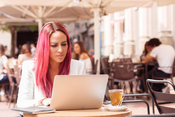 Young woman concentrated using a laptop at a table outside a cafe