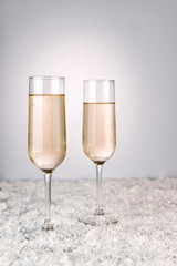 Two champagne glasses on light snow background. New Year and Christmas Celebration. Red baubles, garland, tree ornaments
