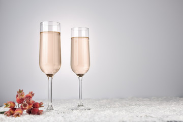 Two champagne glasses on light snow background. New Year and Christmas Celebration. Red baubles, garland, tree ornaments