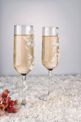 Two champagne glasses on light bokeh background. New Year and Christmas Celebration. Red baubles, berries, garland, tree ornaments and gift boxes