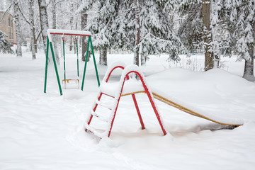 A swing, a ladder covered with snow. A swing and a ladder on the Playground look bright in the snow.