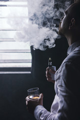 Pensive looking male in relaxed mood. Man leisure with alcohol and vape in private club, bad habits. Luxury life with whiskey and smoking, dark place background