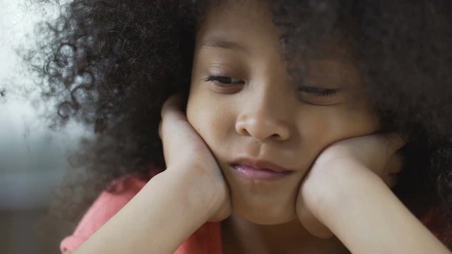 Lonesome Afro-American female kid looking up and thinking about friends, closeup