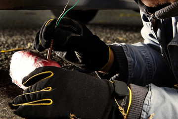 Assassin installing plastic explosive under car outdoor on parking place