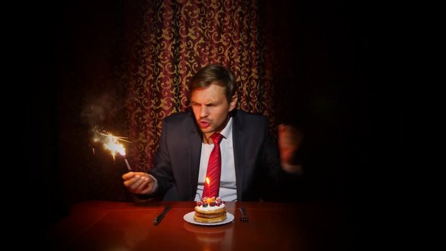 a lone man celebrates a holiday, he sits alone at a table with a cake and a candle. 4k, slow motion