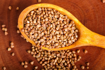 Pile of buckwheat in a wooden spoon  on brown background.