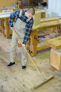 male carpenter in carpentry workshop is sweeping sawdust