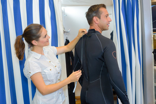 Man trying on wetsuit, woman securing zip