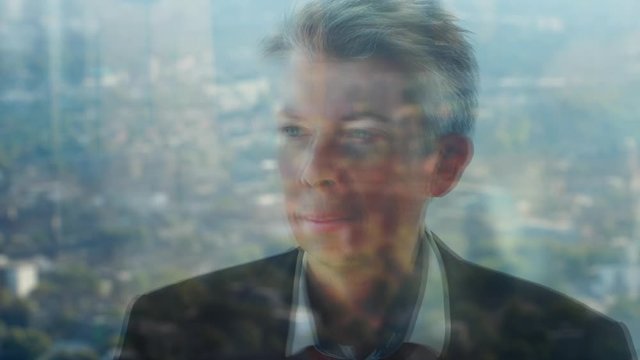 Reflection of a businessman looking out of a window with a city skyline in the background