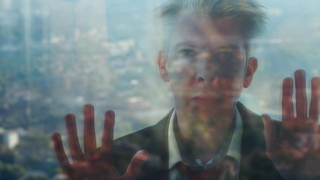 Reflection of a businessman looking out of a window with a city skyline in the background