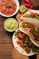 Three Mexican tacos with marbled beef, black Angus and vegetables on old rustic table. Mexican dish with sauces guacamole and salsa in bowls. top view