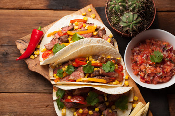 Three Mexican tacos with marbled beef, black Angus and vegetables on old rustic table. Mexican dish with sauces guacamole and salsa in bowls. top view