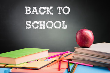 A school teacher's desk with a stack of exercise books colored pencils and green apple. Back to school concept