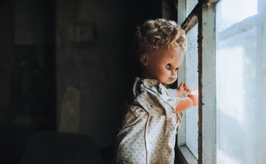 The old doll stands by the window and looks out the window. Nostalgia for better times. The concept...
