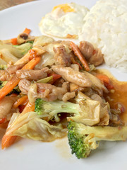 Thai spicy food : A plate of pork stir fry with vegetables and fried egg with rice in white dish on wooden table.  healthy dish.