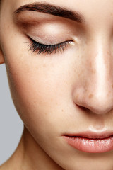 Closeup macro portrait of female face with closed eyes. Human woman half-face  with day beauty makeup. Girl with perfect skin and freckles