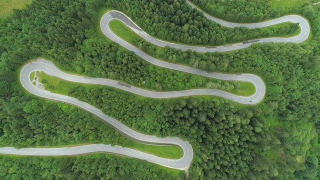 AERIAL, TOP DOWN: Bikers on motorcycles speeding through sharp turns on winding zig zag serpentine road. Blue sports car driving on winding mountain highway through beautiful lush green spruce forest