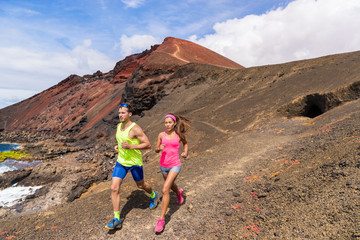 Running trail runners couple training on mountain. Ultra run race athletes training together on volcanic mountains nature landscape in summer outdoors. Difficult rocky terrain.