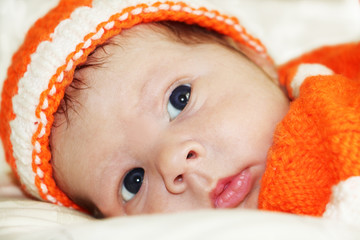 Pensive baby. Portrait of meditative newborn baby with beautiful blue eyes  in orange knitted costume on white fur blanket. 