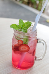 Refreshing iced strawberry lemonade in mason jar on a green nature background. Summer fresh concept.