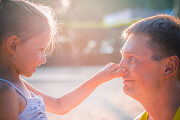 Cute little girl and her handsome father are talking and smiling. Daughter is touching his dad's nose.
