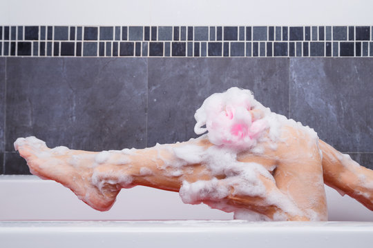 close up of woman washing leg with sponge in bathtub